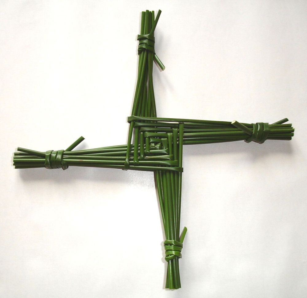 Croix à quatre branches décalées, tressée en joncs verts, sur fond clair