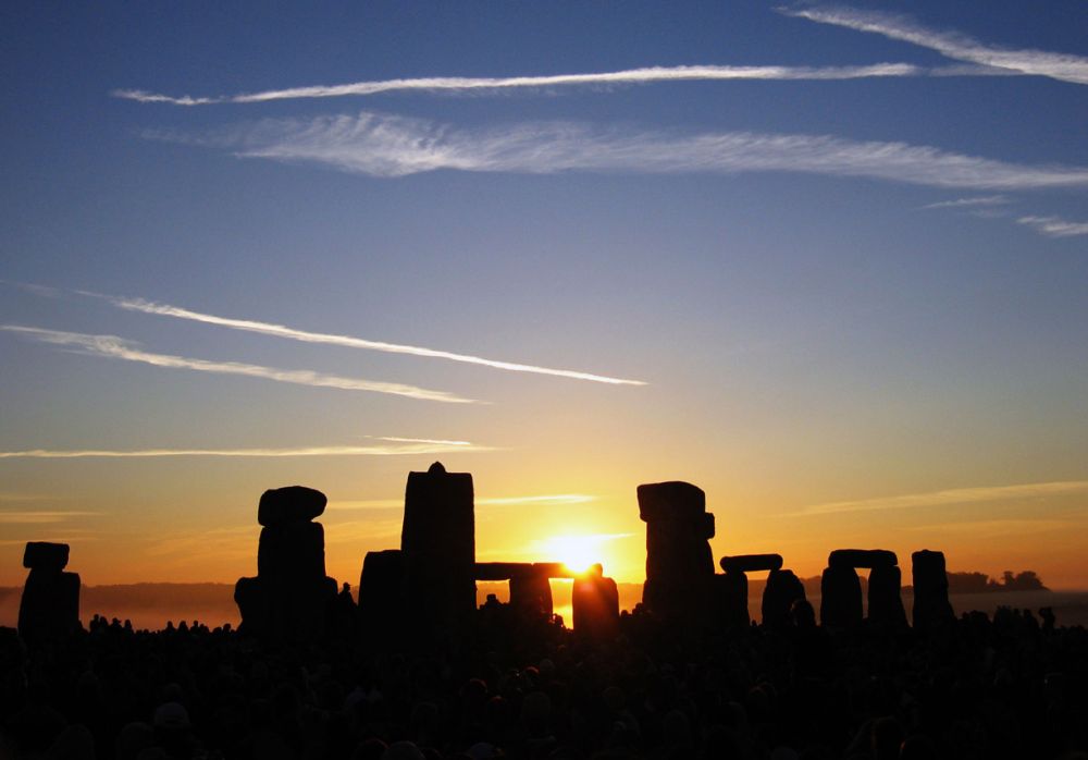 Silhouettes des mégalithes de Stonehenge à contre-jour devant le soleil levant, foule au premier plan